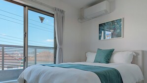 A bedroom with a large bed, a window with blinds, an air conditioning unit, and a painting on the wall. - The FLOW Okinawa (Chatan)