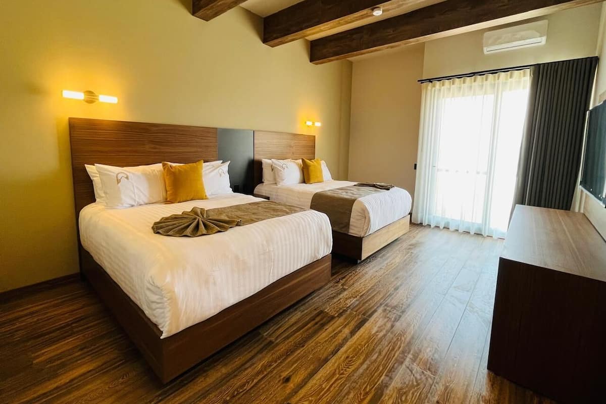 A hotel room with two beds, wooden flooring, and a large window with curtains.