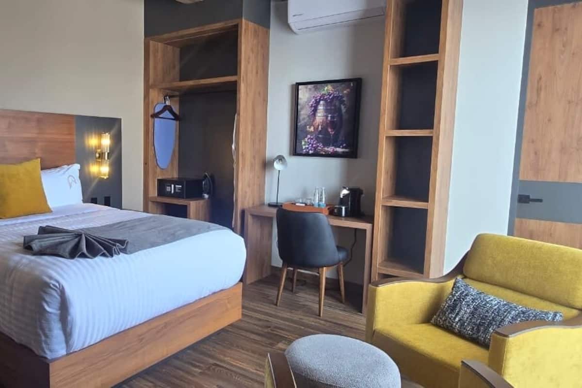 A modern hotel room with a large bed, bedside tables, a desk, a chair, and built-in shelving.