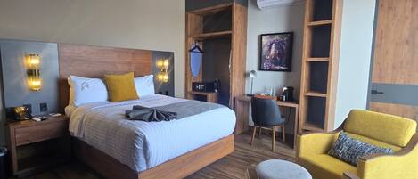 A modern hotel room with a large bed, bedside tables, a desk, a chair, and built-in shelving.