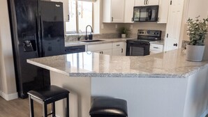 Een moderne keuken met witte kasten, een zwarte koelkast, een roestvrijstalen magnetron en een granieten aanrecht.