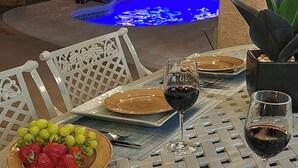 Een eettafel gedekt met borden, bestek en glazen, met een zwembad op de achtergrond.