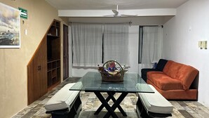 Een eethoek met een glazen tafel, twee banken, een plafondventilator en een bank.