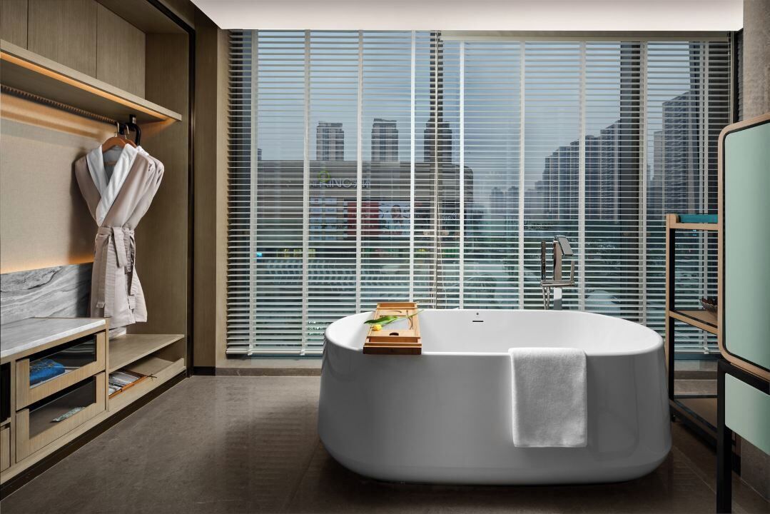A modern bathroom with a freestanding bathtub, a robe rack, and a view of the city through large windows.