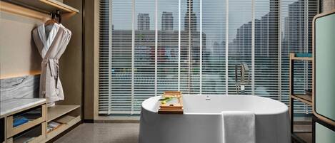 A modern bathroom with a freestanding bathtub, a robe rack, and a view of the city through large windows.