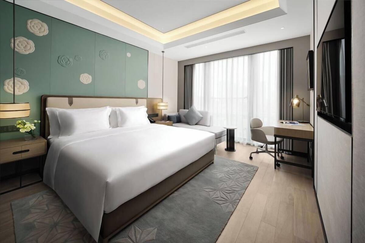 A modern hotel room with a large bed, a desk, and a seating area.