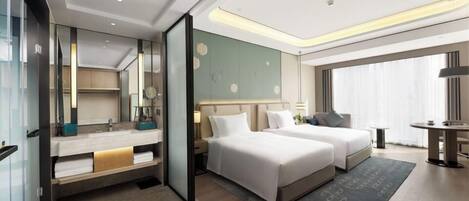 A modern hotel room with two beds, a large mirror, a vanity with a sink, and a large window with curtains.