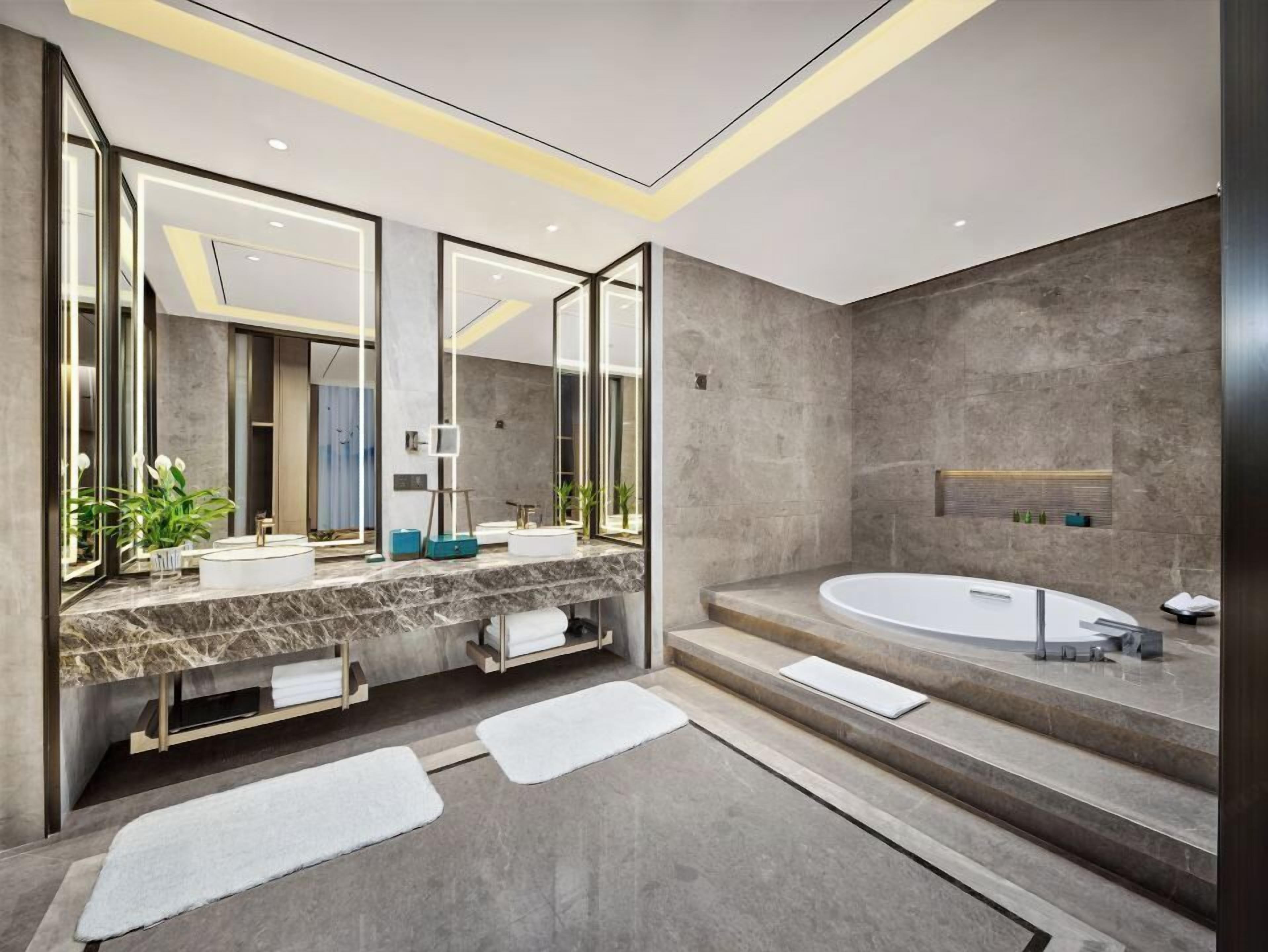Ein modernes Badezimmer mit einem großen Spiegel, zwei Waschbecken, einer Badewanne und einer Marmorarbeitsplatte.
