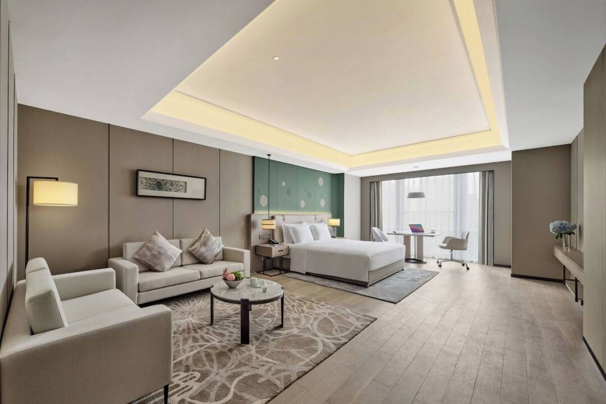 A modern hotel room with a large bed, a sofa, a desk, and a chair.