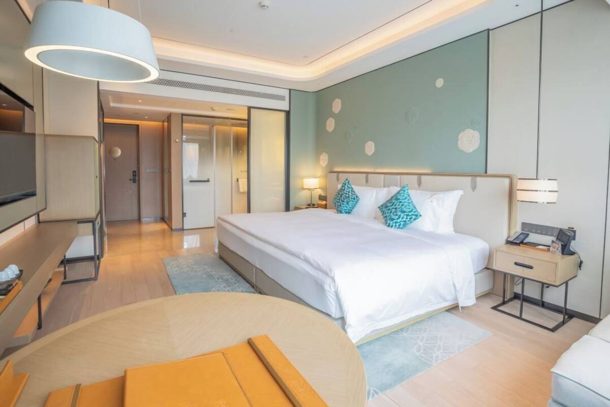 A modern hotel room with a large bed, bedside tables, a TV, and a seating area.