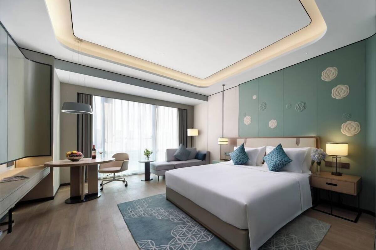A modern hotel room with a large bed, a desk, a chair, and a small table.