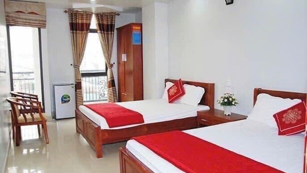 Habitación de hotel con dos camas, un armario de madera, un escritorio, una silla y un refrigerador pequeño.