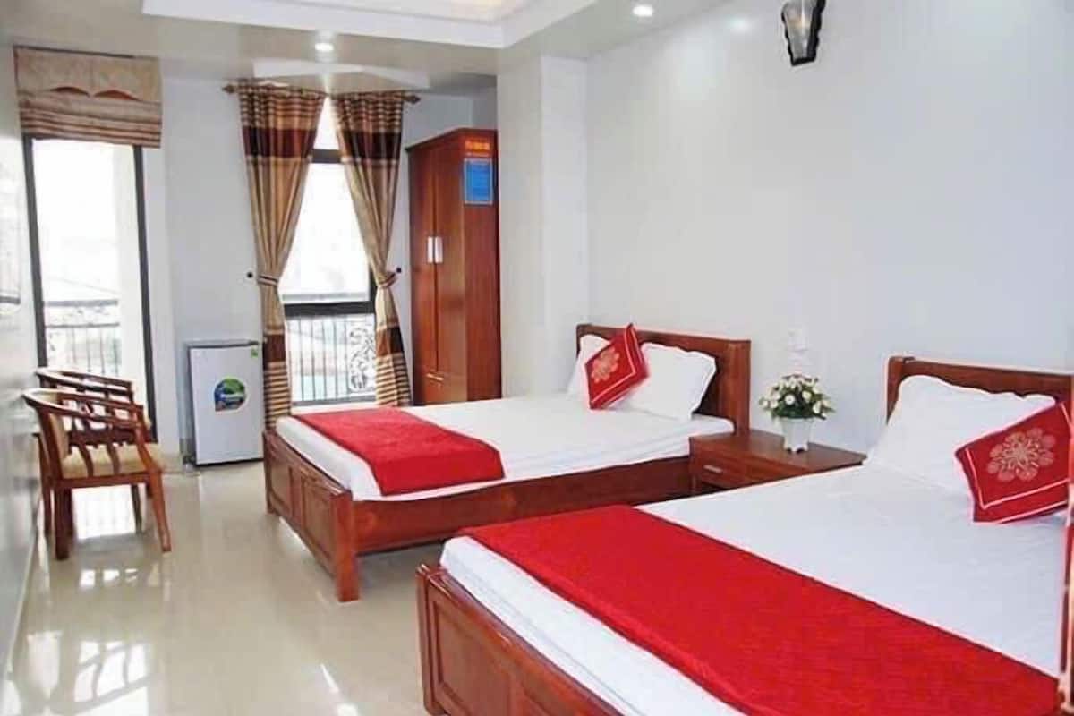 Habitación de hotel con dos camas, un armario de madera, un escritorio, una silla y un refrigerador pequeño.