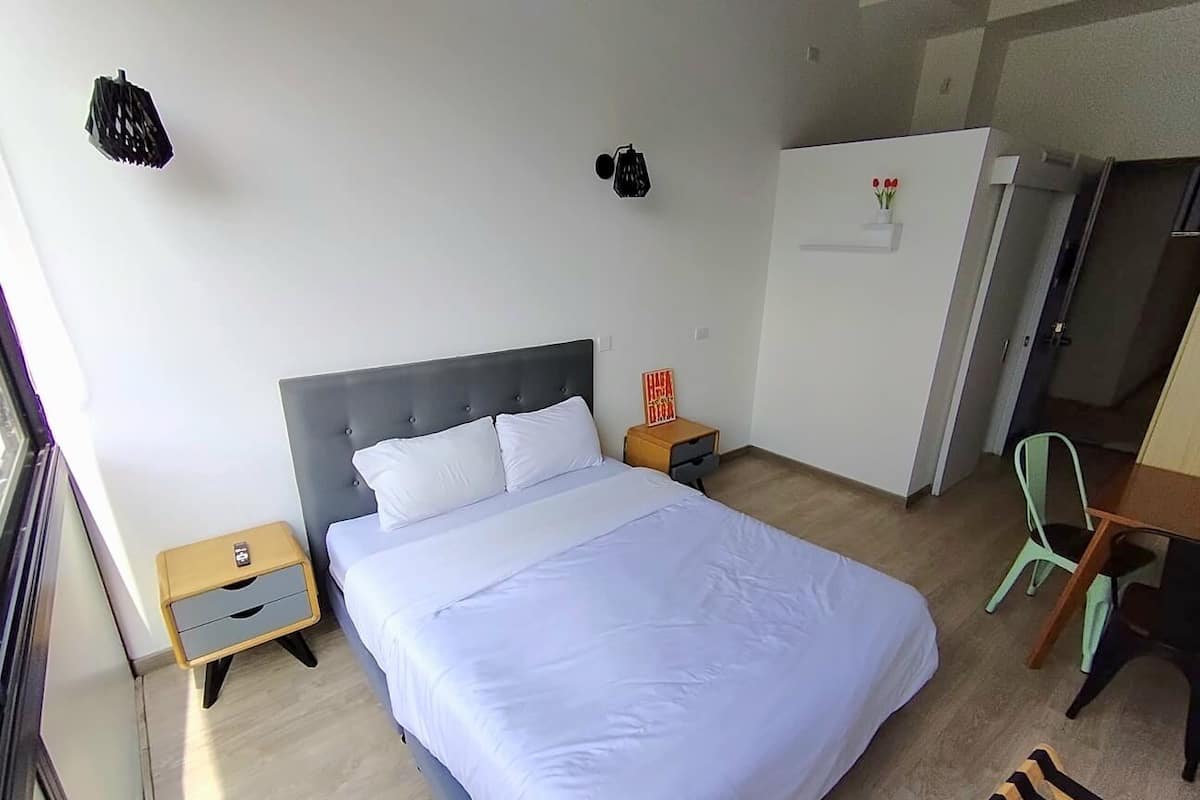 A bedroom with a bed, a nightstand, a desk, and a chair.