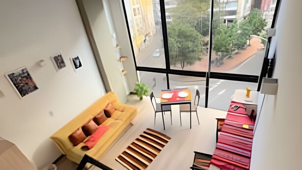 A modern apartment with a large window, a sofa, a dining table, and a staircase. - Tu hogar en Chapinero alto te espera (Bogotá)