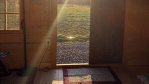 A wooden cabin with a large window and a door, offering a view of a grassy field and a clear sky. - Shawnee Wine Trail Farm Stay (Makanda)