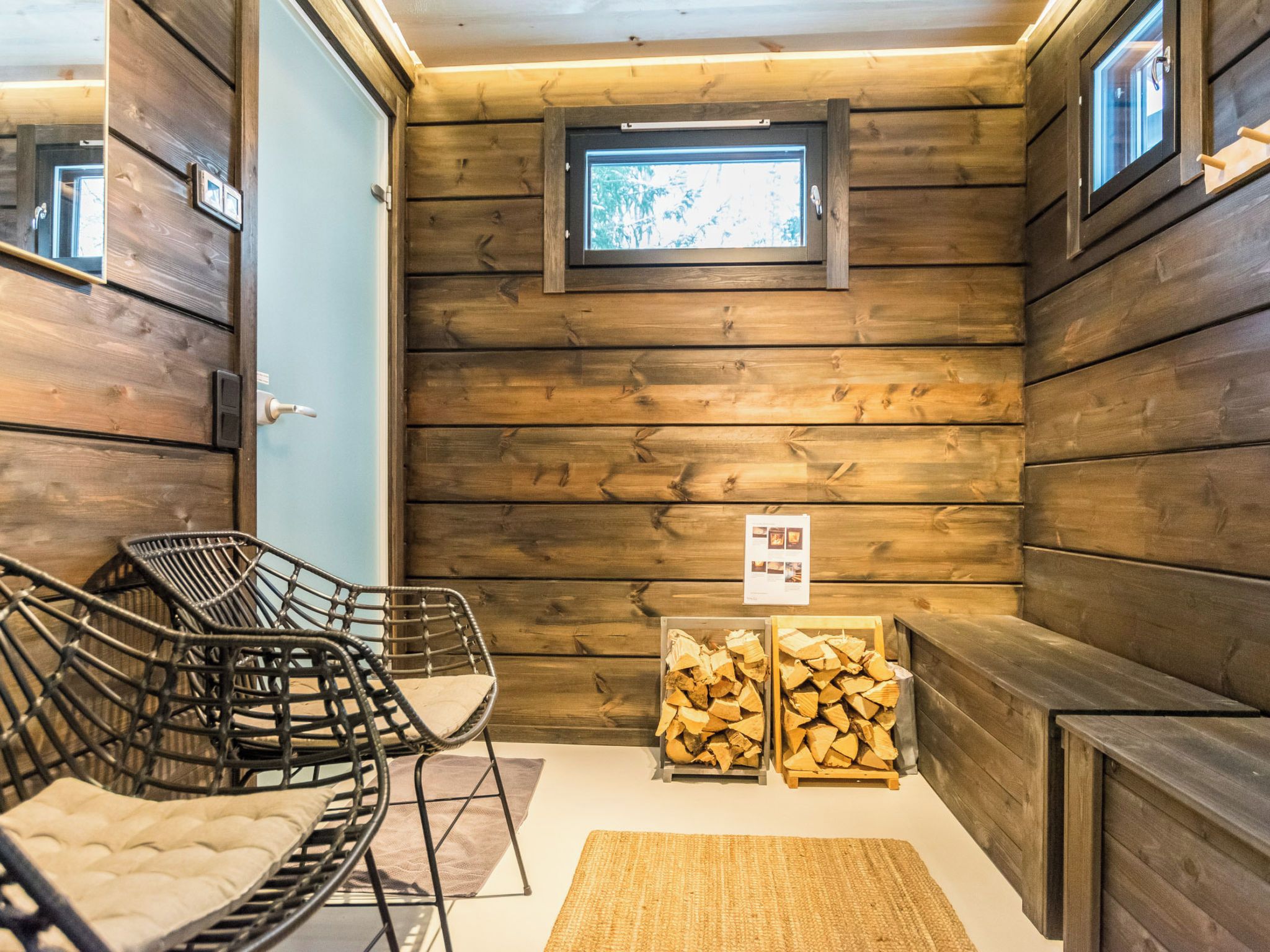 Ein Interieur einer Holzhütte mit Holzwänden, einem Fenster, einem Sessel, einer Bank und einem Holzstoß.
