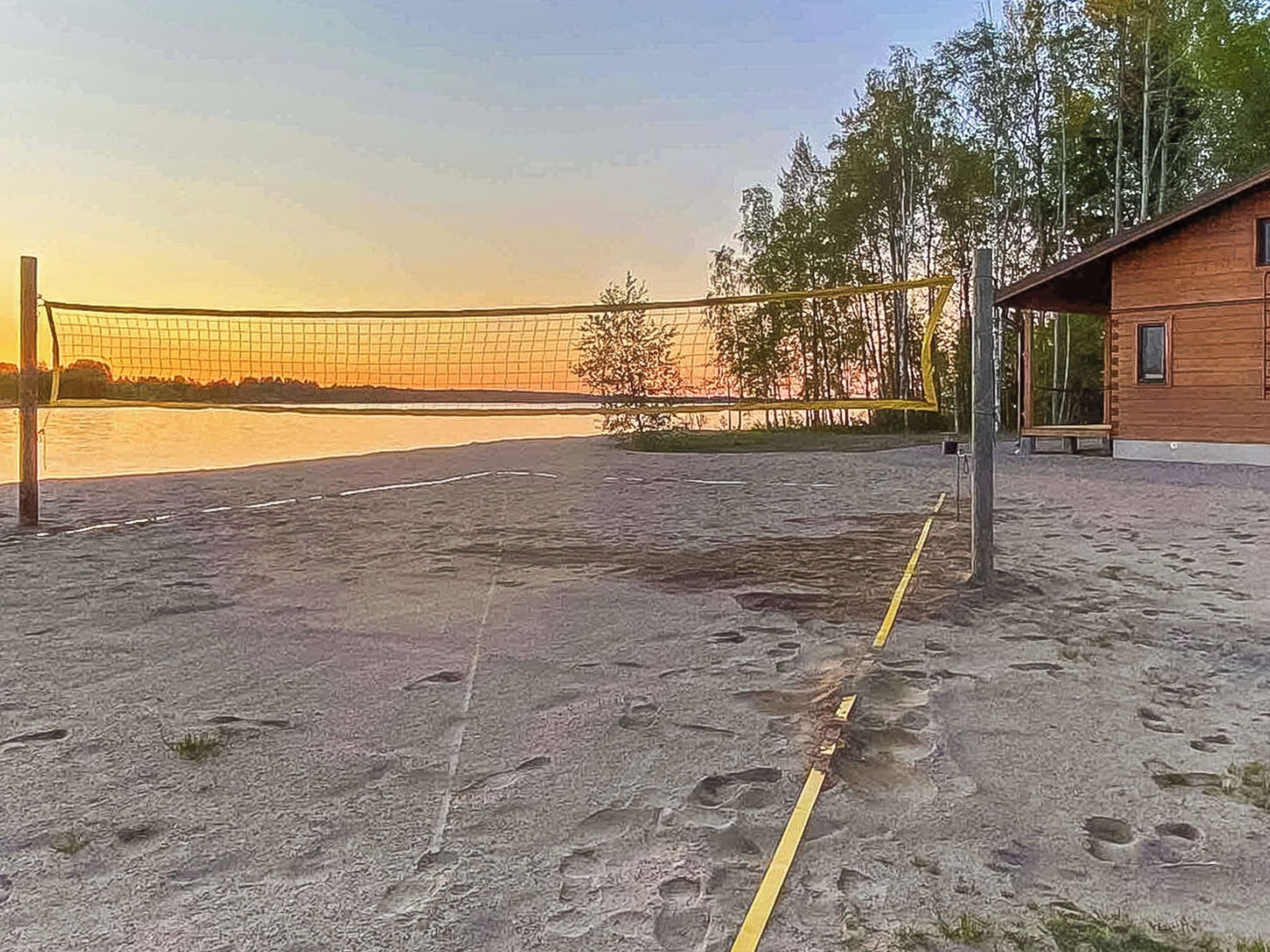 A beach volleyball court with a net, adjacent to a building with a bench and a window.