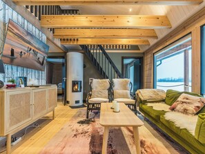 A modern living room with a fireplace, wooden beams, a sofa, and a dining table. - Villa rantakoivikko by Interhome (Karvia)