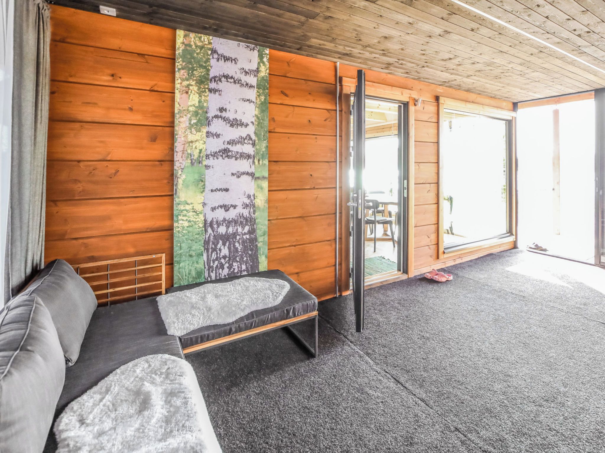 A room with a wooden wall, a sofa, a bench, and a large window.