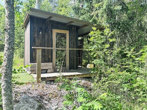 Una cabaña rústica con puerta de madera, un pequeño porche y vistas del bosque circundante.