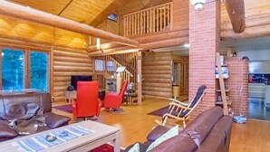 A spacious log cabin interior with a wooden staircase, a dining area, and a living room with leather sofas and a coffee table.