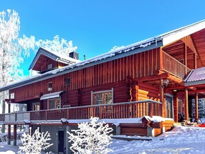 En stuga byggd av trä med en balkong, ett snötäckt tak och en klarblå himmel.