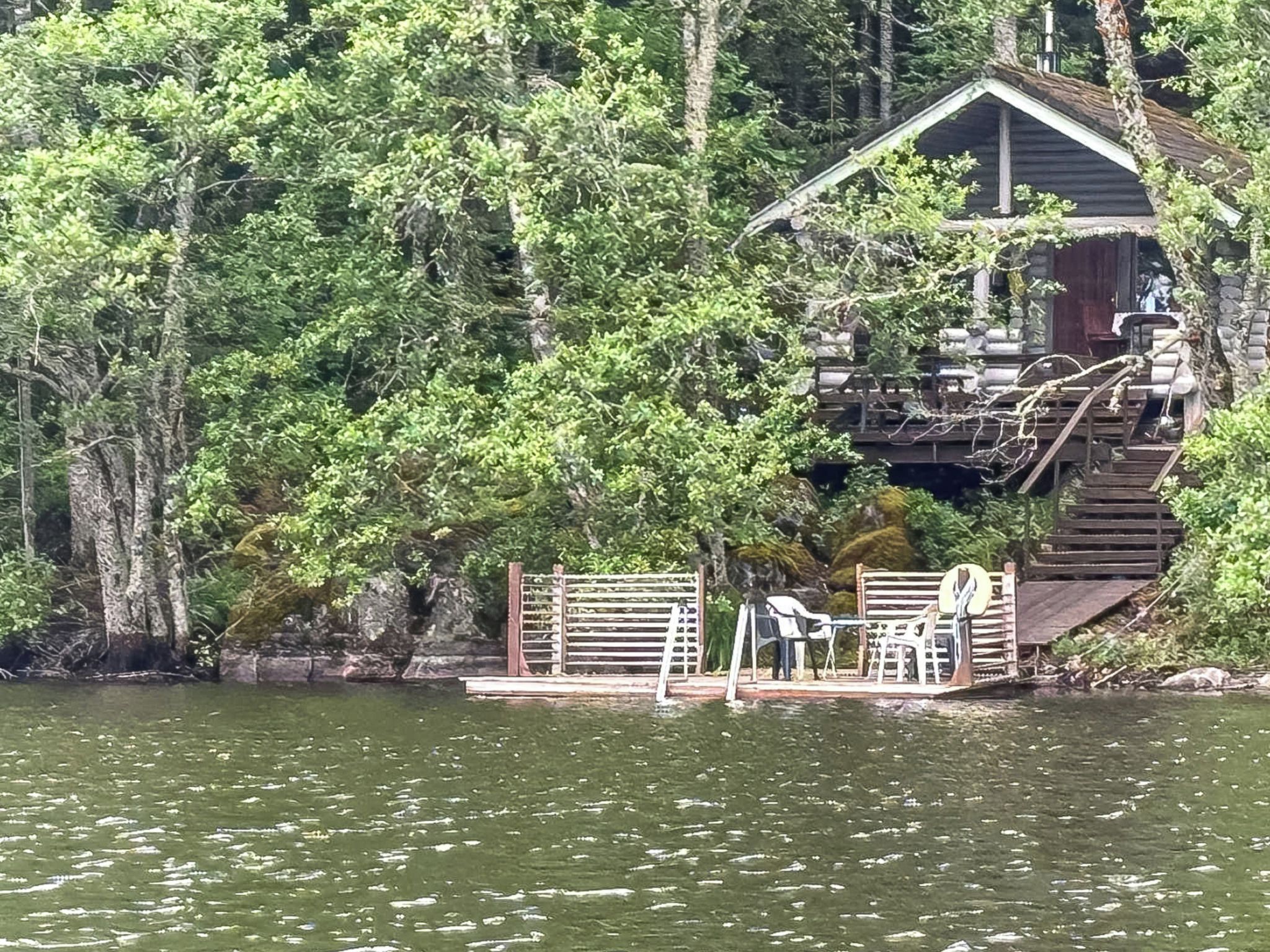 A cabin with a dock extending into a lake, surrounded by dense forest.