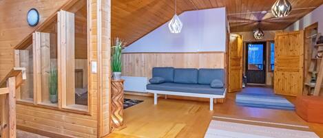 A wooden interior with a sofa, a staircase, and a hanging light fixture.