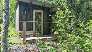 A rustic cabin with a wooden door, a small porch, and a view of the surrounding forest.