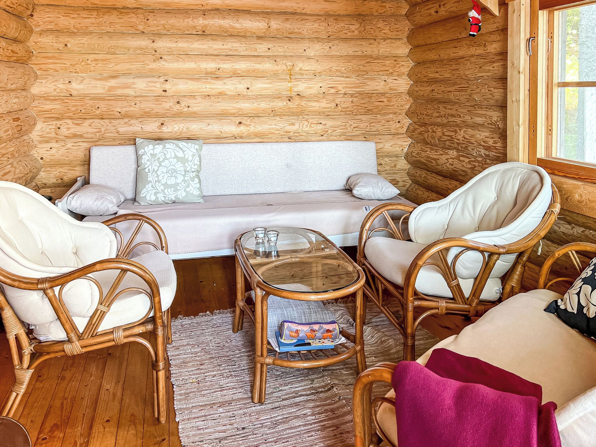 A cozy cabin interior with a sofa, two wicker chairs, a glass table, and a window with a view.