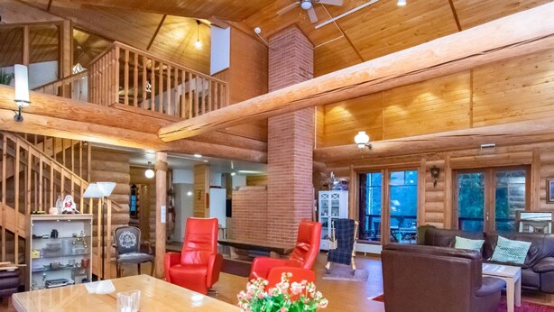 A spacious wooden interior with a high ceiling, a central dining table, and a staircase leading to an upper level.