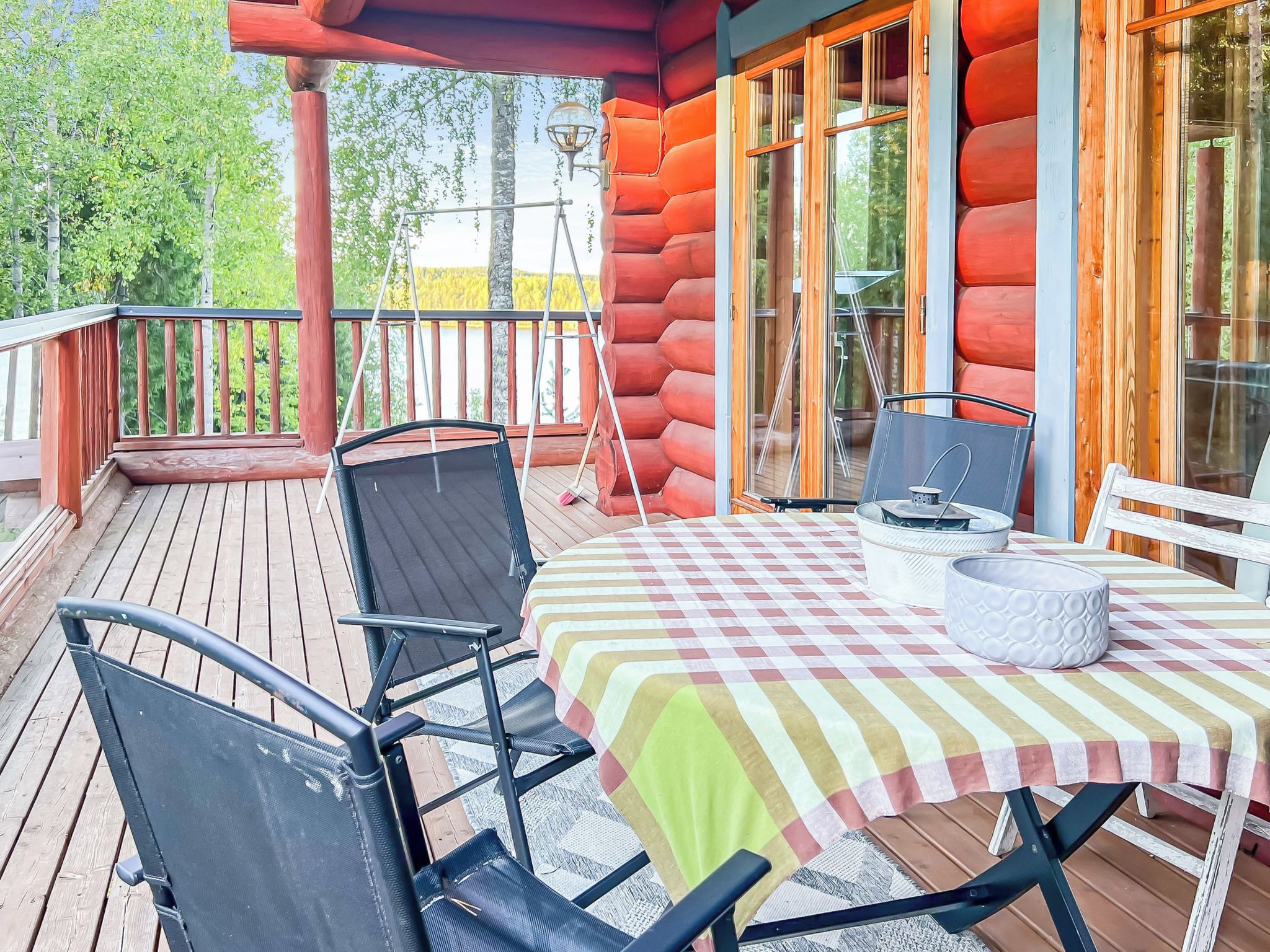 En träveranda med ett bord och stolar, en lykta och utsikt över träd.