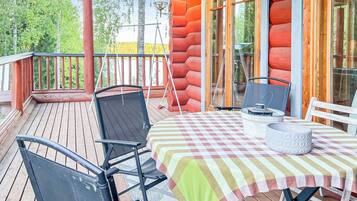 En träveranda med ett bord och stolar, en lykta och utsikt över träd.