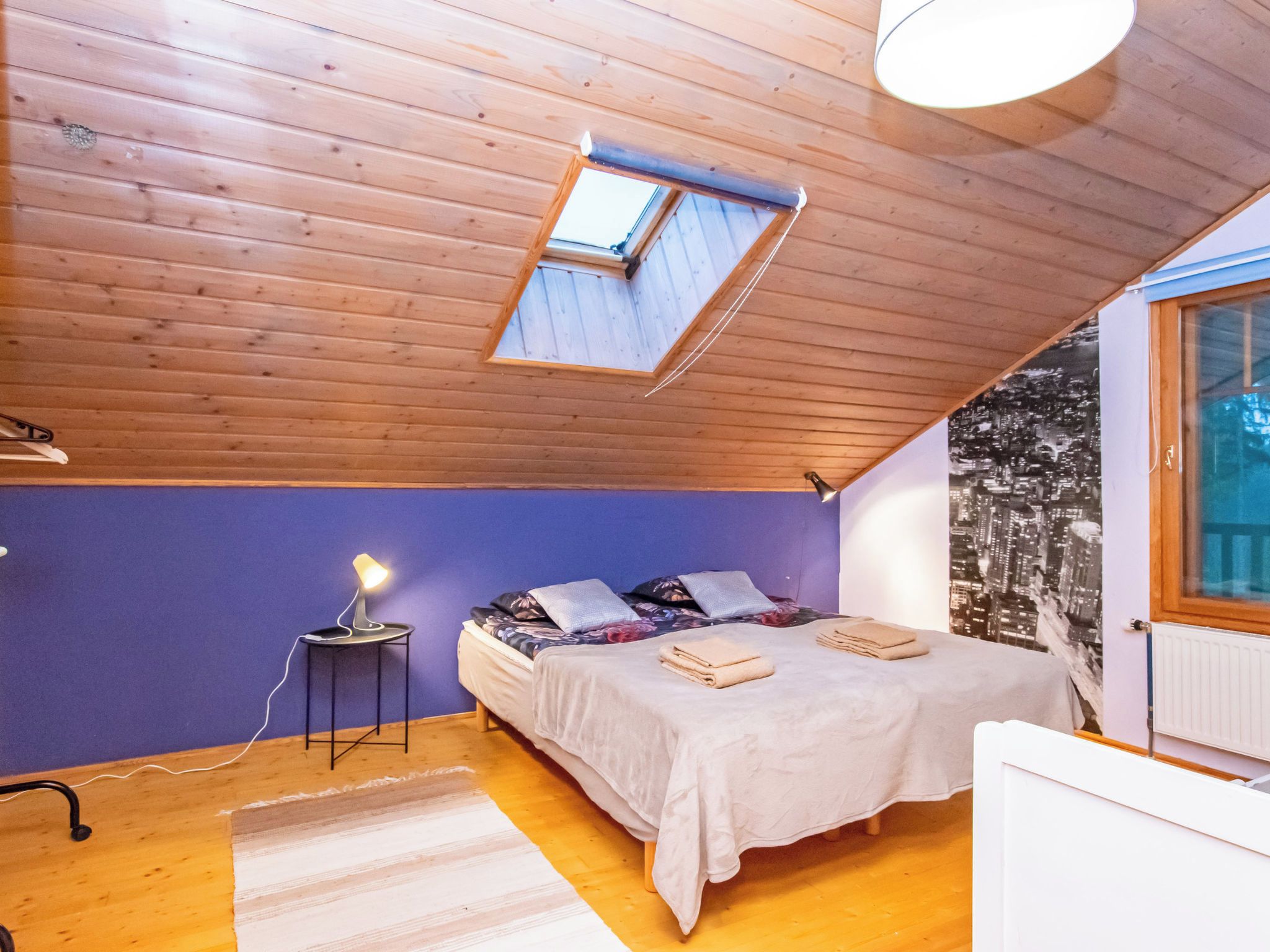 Ein Schlafzimmer mit Dachfenster, einem Bett mit Kissen, einer Nachttischlampe und einer Heizung.