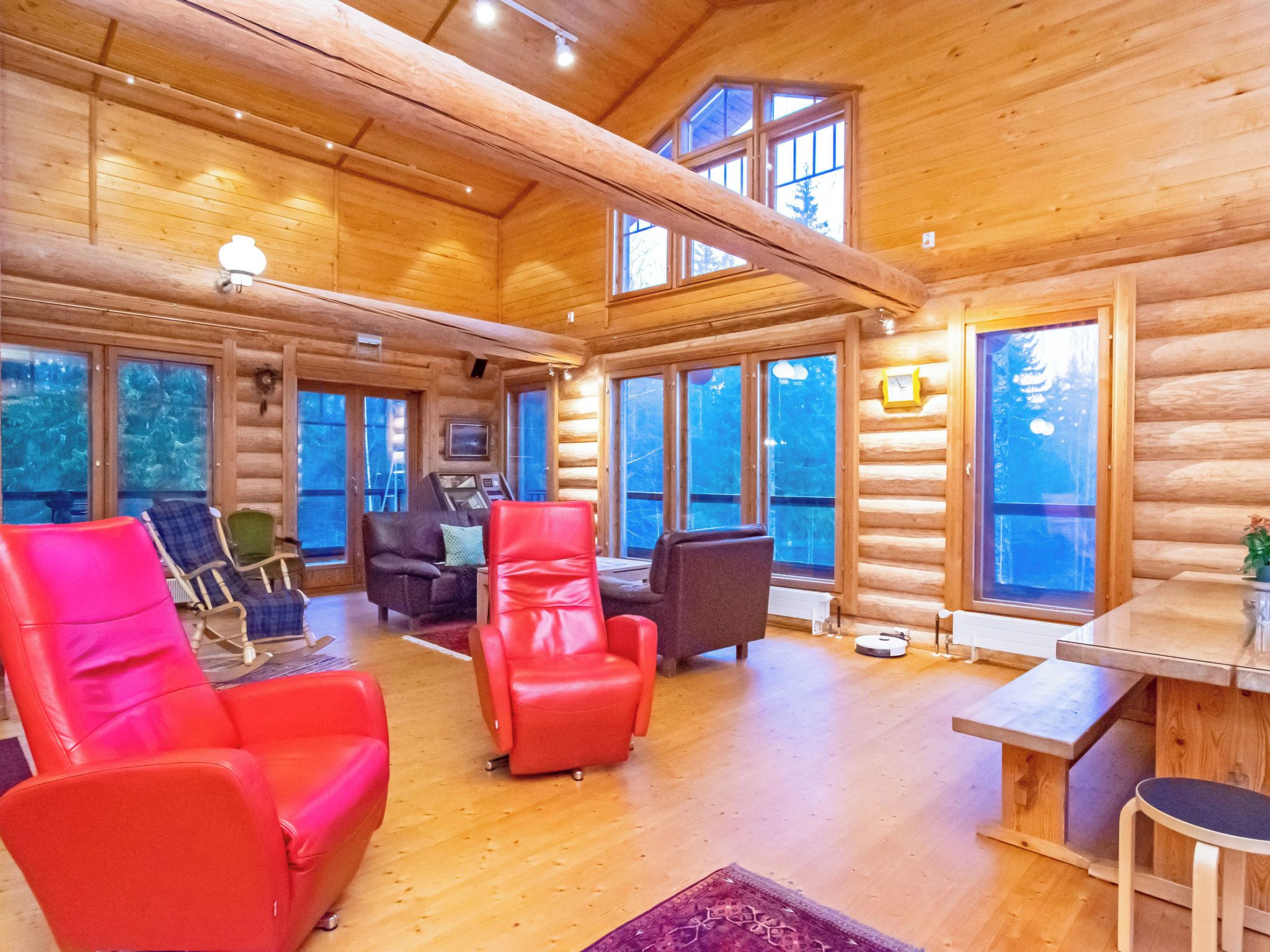 A log cabin interior with a high ceiling, wooden walls, and large windows.