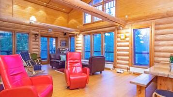 A log cabin interior with a high ceiling, wooden walls, and large windows.