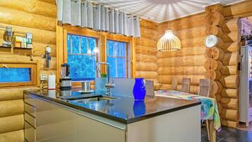 Interior de uma cabana de toras com ilha de cozinha, paredes de madeira e área de jantar.