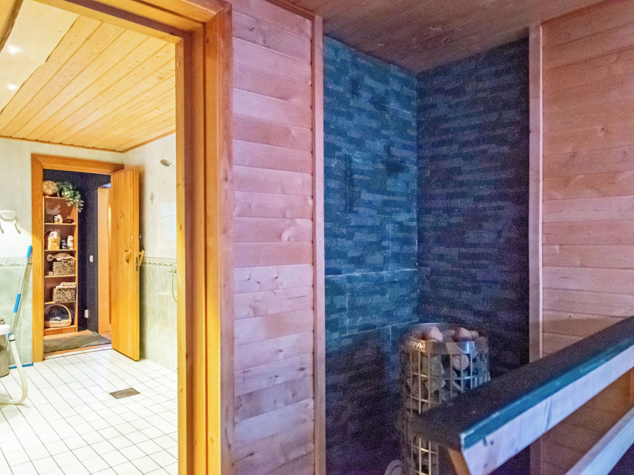 A wooden interior with a tiled floor, a visible kitchen area with a sink and a metal container, and a doorway leading to another room.