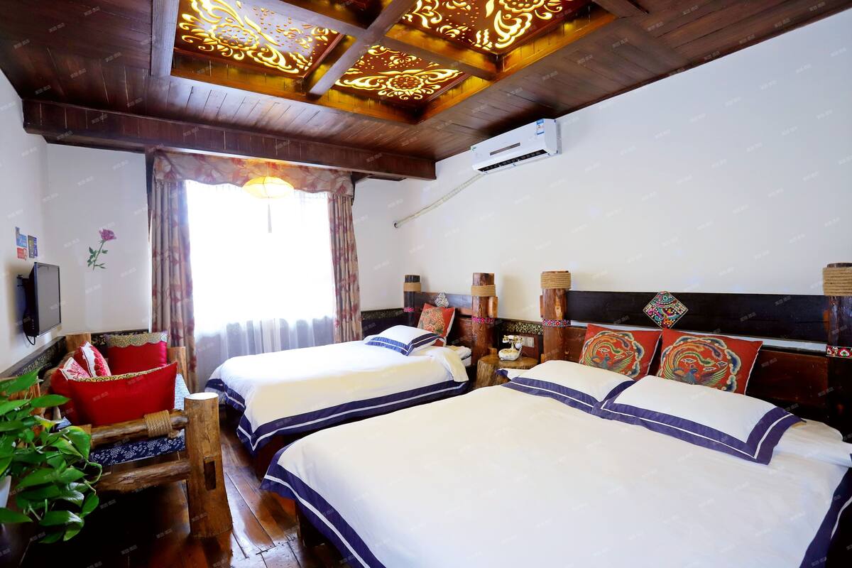 Habitación de hotel con dos camas, cabeceros de madera decorativos, un televisor montado y una ventana con cortinas.