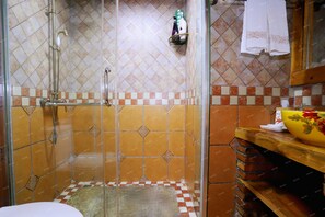 A bathroom with a shower, tiled walls, a sink, and a wooden shelf with toiletries. - Butterfly Loves Flower Inn (Zhangjiajie)