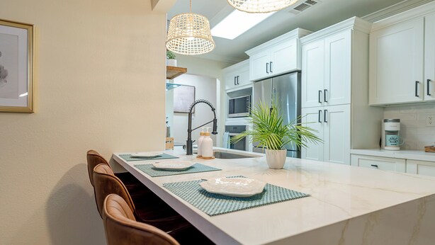 Une cuisine moderne avec des meubles blancs, un îlot en marbre et des luminaires suspendus.