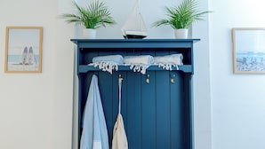 Un mur peint en bleu, sur lequel est fixée une étagère portant deux plantes en pot, un tableau encadré et une maquette de voilier.