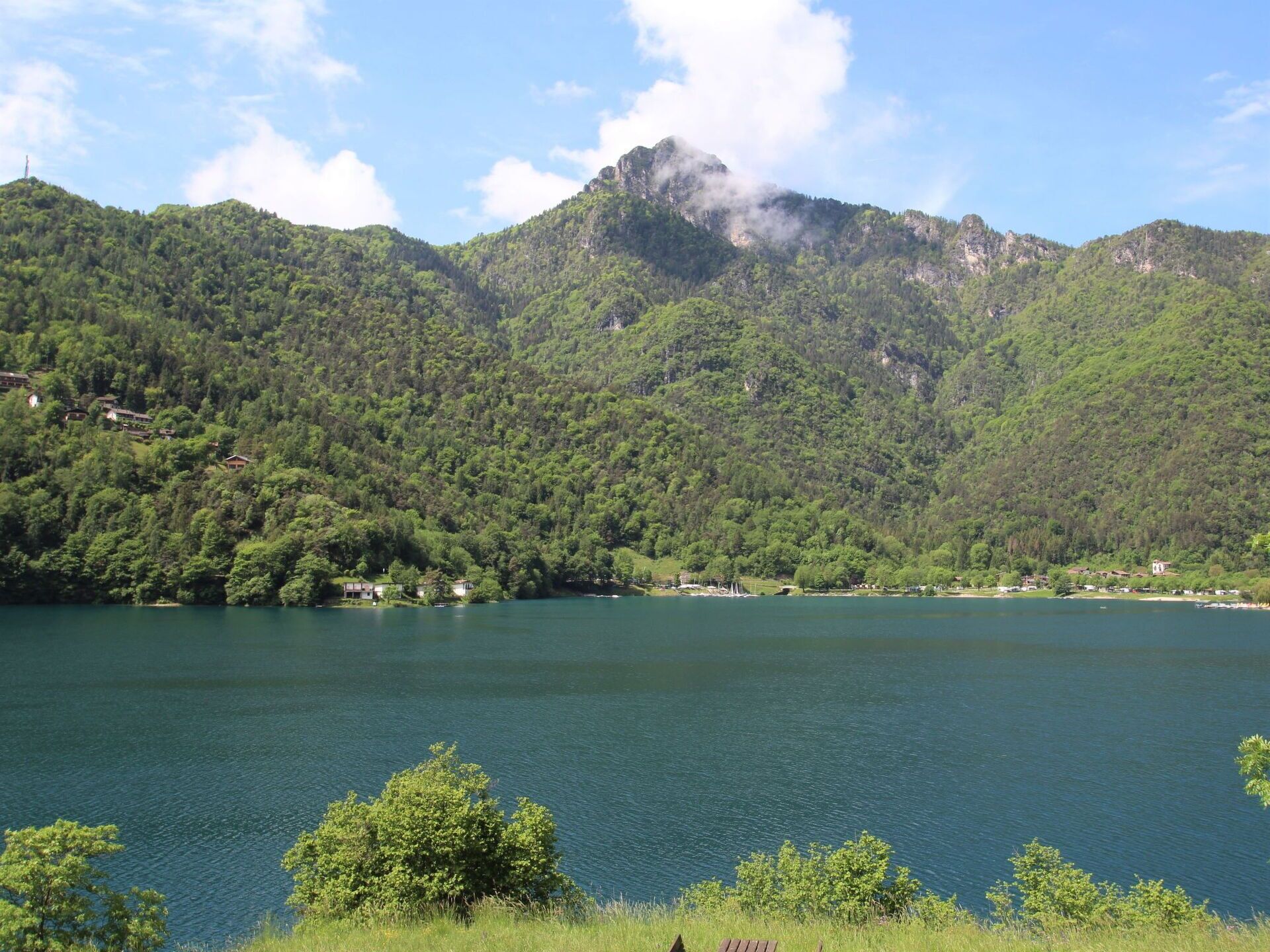 Un paysage montagneux avec un lac, entouré d’une végétation luxuriante et de quelques bâtiments dispersés.