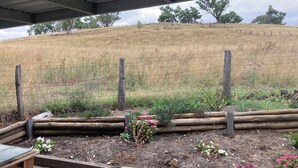 Un espace extérieur abrité, doté d’une clôture en bois, d’un portail en métal et, au fond, d’une colline couverte d’herbe.