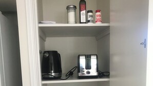 Une cuisine équipée d’une machine à café, d’un grille-pain et de divers ustensiles, notamment des assiettes, des bols et une planche à découper.