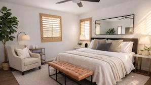 Une chambre à coucher comprenant un lit, une chaise, un banc, un grand miroir et un ventilateur de plafond.