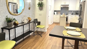Une cuisine moderne avec des meubles blancs, des appareils en acier inoxydable et un coin repas comprenant une table noire et des chaises jaunes.