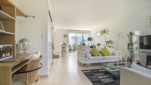 Una sala de estar moderna con un sofá blanco, una mesa de centro de vidrio y un ordenador portátil sobre un escritorio de madera.