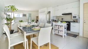 Una cocina moderna con armarios blancos, un comedor con mesa de vidrio y una planta en maceta.